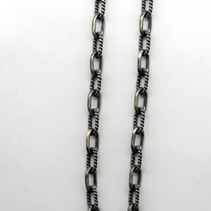 May include: A silver chain necklace with a twisted rope design. The chain is made of oval links.