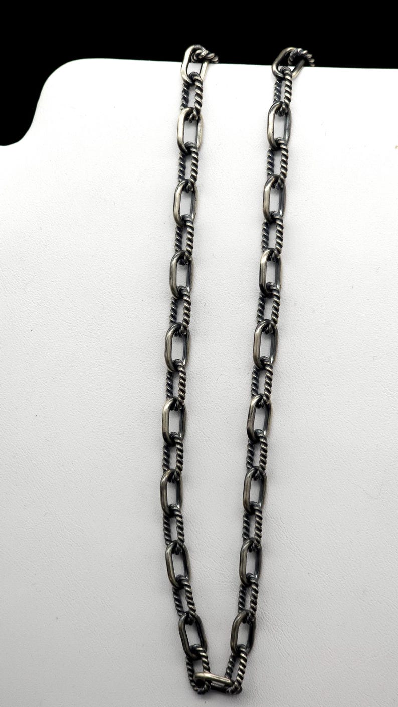 May include: A silver chain necklace with a twisted rope design. The chain is made of oval links.