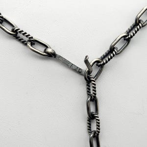 May include: Close-up of a silver chain necklace with a twisted rope design. The chain has a lobster clasp and is marked "925 Italy A.J.C."
