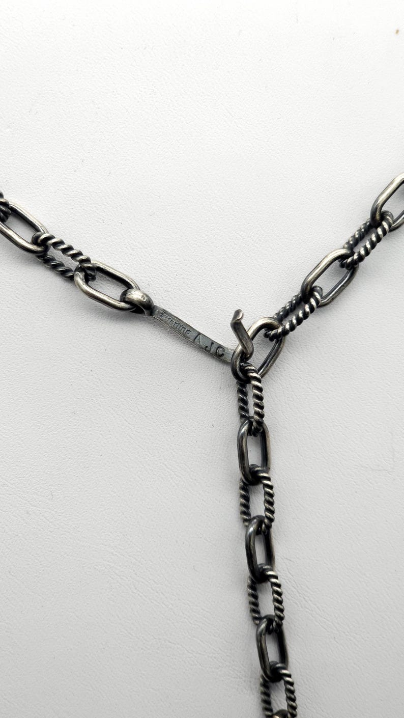 May include: Close-up of a silver chain necklace with a twisted rope design. The chain has a lobster clasp and is marked "925 Italy A.J.C."