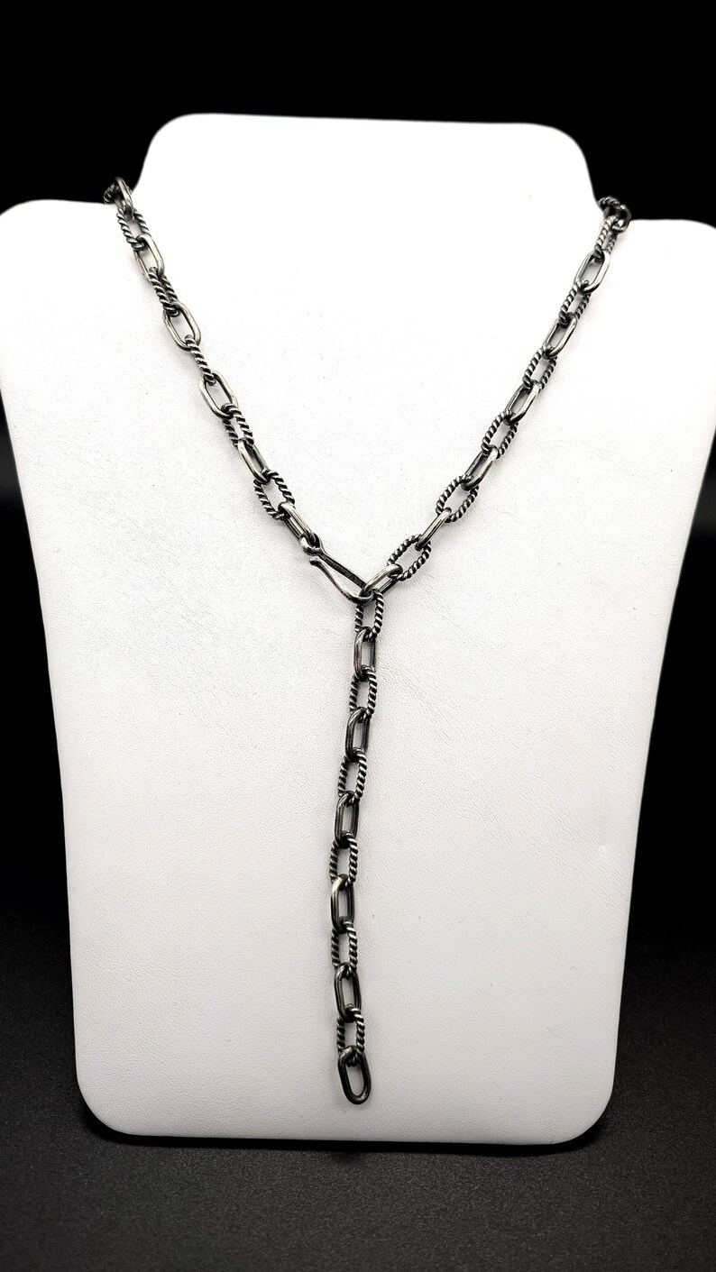May include: A silver chain necklace with a twisted design. The chain is made of oval links and has a lobster clasp.