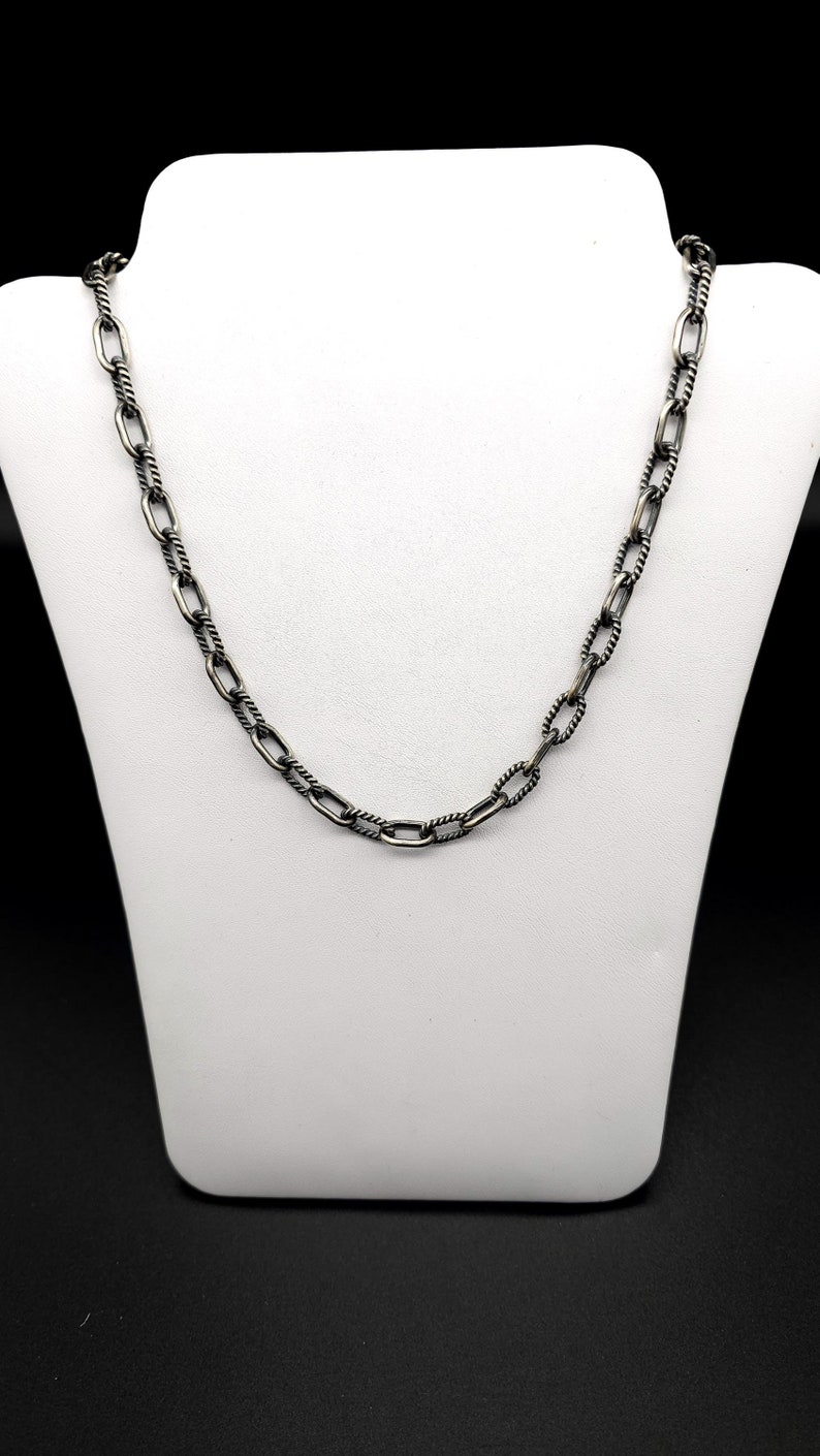 May include: A silver chain necklace with a twisted rope design. The chain is made of oval links.