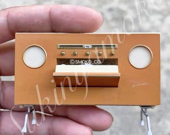 Può includere: Un sistema stereo vintage in miniatura di colore arancione e bianco con un giradischi, altoparlanti e una porta scorrevole. Il sistema stereo è su una superficie bianca.