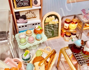 Op de afbeelding: Een miniatuur bakkerspeelset met een houten vitrine, een etalage met verschillende miniatuurgebakjes en een bord met de tekst "Sumikko Patisserie".