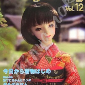 Op de afbeelding: Een pop in een rood-oranje kimono met een zwarte obi staat op de cover van "Dolly Dolly Vol. 12". De pop heeft kort, donker haar. Japanse tekst is zichtbaar.