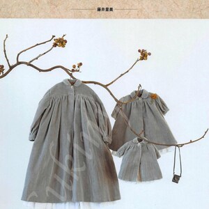 May include: Three gray dresses of varying sizes hang from a branch against a white background. The dresses have a button-up design and a white trim at the hem. The word "HANON" is displayed at the top of the image.