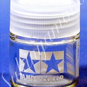 May include: A clear glass jar with a white lid. The jar has two blue stars and the text "TAMIYA COLOR" printed on the side.