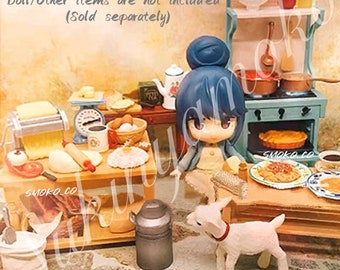 May include: A miniature dollhouse kitchen set featuring a blue and white stove, a wooden table, a rolling pin, a pasta maker, a scale, a bowl of eggs, a loaf of bread, a milk jug, a goat figurine, and a doll wearing a blue dress. The set is made of wood and plastic and is designed for children to play with.