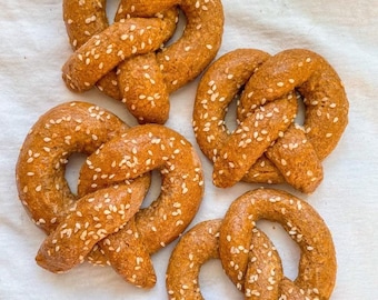 Peut inclure: Quatre bretzels moelleux avec des graines de sésame sur un fond de lin blanc. Les bretzels sont disposés en cercle, les pointes des bretzels étant dirigées vers le centre du cercle.