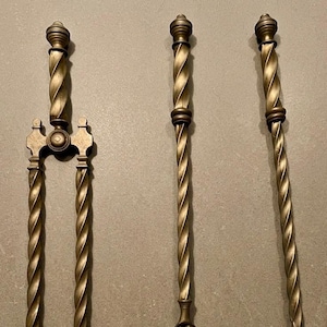 May include: A set of three brass fireplace tools featuring twisted handles. The set includes a pair of tongs with a U-shaped base, a shovel with a scalloped edge design, and a long poker with a pointed tip. Each tool has a matching spiral design.