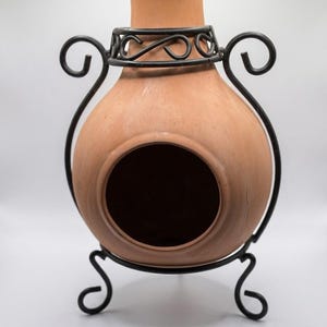 May include: A terracotta chiminea featuring a round body with a large circular opening, a narrow neck, and a black metal stand. The stand includes decorative scrollwork accents that wrap around the neck and base of the clay vessel.