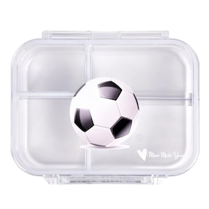 Könnte beinhalten: Eine transparente, rechteckige Brotdose mit einem Fußball-Motiv. Die Brotdose hat ein geteiltes Innenleben und einen Klappdeckel. Der Fußball ist weiß mit schwarzen Fünfecken. Der Text "Mum Made Yum" ist unten rechts aufgedruckt.