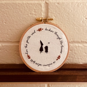 Può includere: Arte di ricamo a cerchio con una citazione sui colori autunnali e un vento gentile che invita attraverso le foglie. La citazione dice: "Come i colori autunnali cadono, come il vento gentile invita attraverso le foglie."