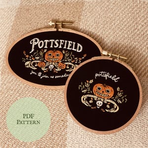 May include: Two black embroidery hoops with wooden frames. The hoops feature a Halloween-themed design with a jack-o'-lantern, skull, and leaves. The text "Pottsfield" and "You'll join us someday" are embroidered on the hoops.