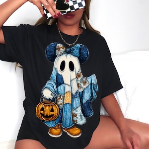 Op de afbeelding: Zwart T-shirt met een cartoon spookontwerp. Het spook heeft Mickey Mouse oren, een blauwe strik en patchwork kleding. Het houdt een pompoen lantaarn vast. Het ontwerp heeft een Halloween thema.