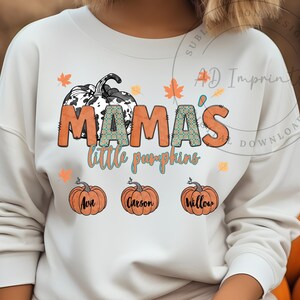 Peut inclure: Sweat-shirt blanc avec un motif graphique représentant une citrouille à imprimé vache avec le texte "Mama's little pumpkins" et trois plus petites citrouilles avec les noms Ava, Carson et Willow.