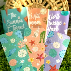 May include: Set of four decorative bookmarks with a beach theme. Each bookmark features a unique design with seashells, starfish, and floral elements. The bookmarks have text that reads "The Summer I Turned", "It's Not Summer", and "We'll Always Have".