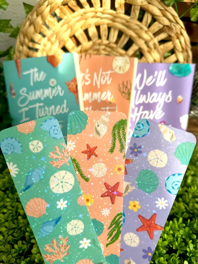 May include: Set of four decorative bookmarks with a beach theme. Each bookmark features a unique design with seashells, starfish, and floral elements. The bookmarks have text that reads "The Summer I Turned", "It's Not Summer", and "We'll Always Have".
