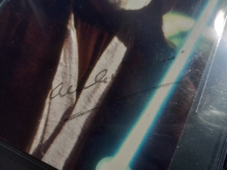 May include: A black and white photograph of a person holding a lightsaber. The person's signature is written in black ink on the photo. The signature reads "Mark Hamill".