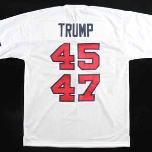 May include: White mesh jersey with the name "TRUMP" in navy blue across the upper back. The numbers "45" and "47" are in red with a navy blue outline. Navy, red, and white stripes adorn the sleeves.
