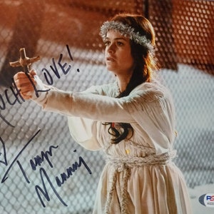 May include: A woman wearing a white dress and a silver headband holds a wooden cross and signs "Much Love!" with a heart and her name.