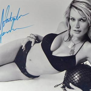 Peut inclure: Photographie en noir et blanc d'une femme portant un haut de bikini noir et un sous-vêtement noir. Elle tient un ballon en maille noire dans sa main droite. La photo est signée "Natasha Henstridge".