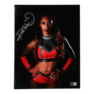 May include: A woman in a red and black wrestling outfit poses for a photo. Her signature is written in silver above her head.