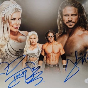 May include: A signed photograph of three professional wrestlers. The wrestlers are standing in front of a gray background. The wrestlers are wearing wrestling attire. The photograph is signed by all three wrestlers. The signatures are in blue ink.