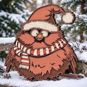 May include: A layered wooden wall art piece depicting a round, red cardinal bird wearing a Santa hat and a red and white striped scarf. The bird has large, wide eyes, a small beak, and textured feather details, crafted from stacked wood layers.