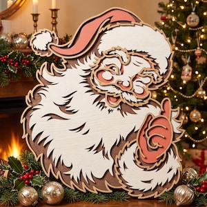 Op de afbeelding: Een gelaagde houten wanddecoratie met een gestileerde kerstman met een witte baard, een rode muts en een rode want. Het ontwerp maakt gebruik van gestapelde uitsparingen voor diepte, met een warm kleurenpalet van wit, crème en gedempt rood.