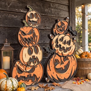 May include: Two layered wooden Halloween decorations featuring stacked carved pumpkins with orange and dark brown tones. The left piece shows four pumpkins in a vertical column, while the right piece displays two larger pumpkins with bat accents.