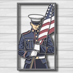 May include: A framed, layered wood cutout depicting a military figure holding an American flag. The figure wears a dark blue uniform with gold details, a white belt, and a white hat. The flag features red and white stripes and a blue field with white stars.