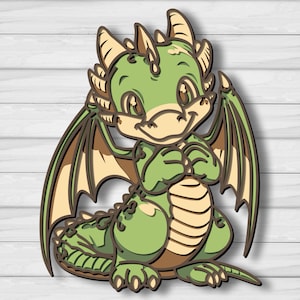 May include: A layered wooden dragon cutout in shades of green and brown. The cartoon dragon has large eyes, wings, and a friendly expression. The dragon is sitting with its hands clasped. The background is a white wood grain.