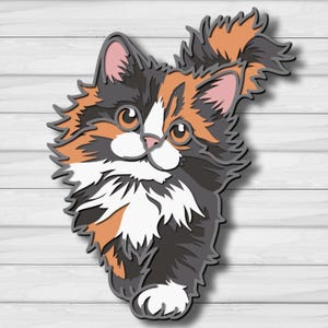 May include: A layered wooden cat cutout with a calico pattern. The cat features orange, black, white, and gray fur, with pink inner ears and large, round eyes. The cutout is set against a white wooden background.