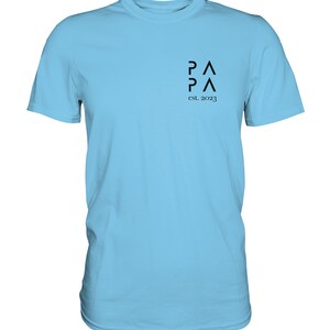 May include: A light blue t-shirt with a black logo that says "PA PA" and "est. 2023".