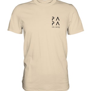 May include: A beige t-shirt with a black graphic design that says "P&Lambda;P&Lambda; est. 2023".
