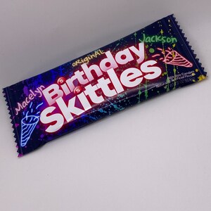 May include: A purple, blue, and green candy bag with the words "original birthday Skittles" in red and white. The bag is decorated with colorful paint splatters and a party horn. The bag is labeled with the name "Macelyn Jackson" and the weight "1.7 oz (61g)".