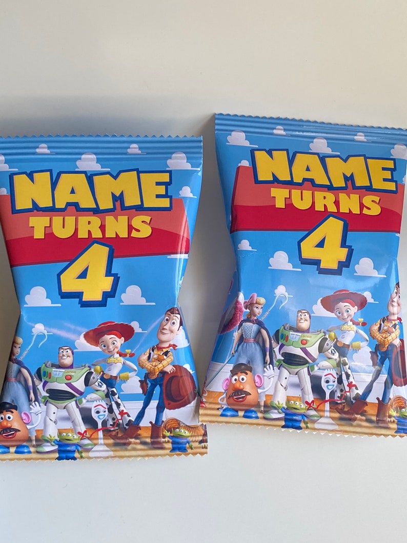 Puede incluir: Dos bolsas de regalo azules y amarillas con tem&aacute;tica de Toy Story. Las bolsas presentan a los personajes Woody, Buzz Lightyear, Jessie y otros. Las bolsas tienen el texto "NAME TURNS 4" impreso en ellas.
