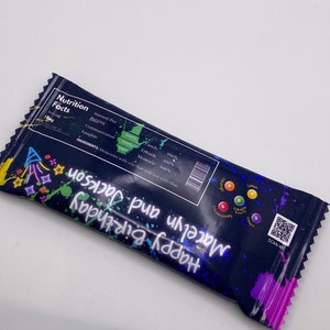 May include: A blue and black birthday party favor bag with colorful paint splatters. The bag has a QR code and the text "Happy Birthday Macelyn and Jackson".