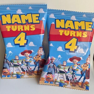 Puede incluir: Dos bolsas de fiesta azules y rojas con tem&aacute;tica de Toy Story. Las bolsas muestran el texto "NAME TURNS 4" e im&aacute;genes de Woody, Buzz Lightyear, Jessie y otros personajes de la pel&iacute;cula.