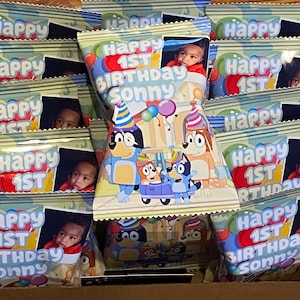 May include: A stack of small, colorful, cellophane bags with a cartoon dog design. The bags have a photo of a young child and the text "Happy 1st Birthday Sonny".