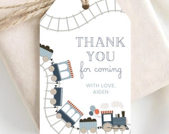 May include: A rectangular white gift tag with a hole at the top and twine, featuring a gray train track illustration, blue and red train cars, and the text THANK YOU for coming WITH LOVE, AIDEN. The design includes a steam engine and balloons.