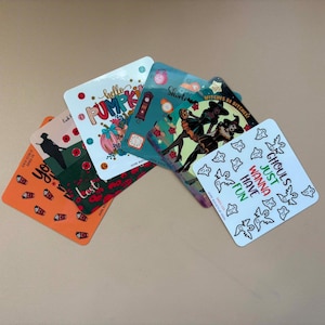 May include: A collection of five square laminated savings challenge cards featuring various seasonal designs. The cards display colourful illustrations of pumpkins, witches, ghosts, and poppies, along with printed text and currency symbols.