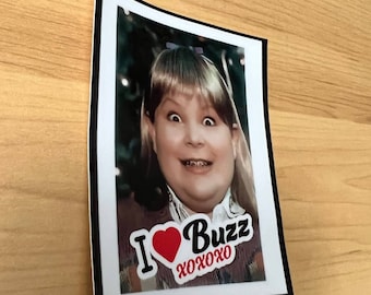 Puede incluir: Una foto enmarcada de una niña con un corazón rojo y el texto "I love Buzz xoxo" impreso en ella.