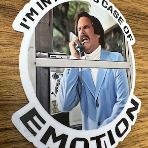 May include: A white sticker with a black circle and the text "I'm in a glass case of emotion" around the edge. Inside the circle is a photo of a man in a blue suit talking on a phone. The man has a mustache and is looking at the phone.