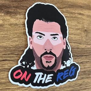 May include: A sticker featuring a cartoon illustration of a man with a black mullet and a white and blue striped mask. The text "ON THE REG" is written in red, white, and blue on a black background.