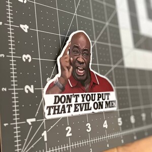 May include: A sticker featuring a close-up of a man with a serious expression, pointing his finger and saying "DON'T YOU PUT THAT EVIL ON ME!"