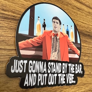 May include: A round sticker with a black background and white text that reads "JUST GONNA STAND BY THE BAR, AND PUT OUT THE VIBE." The sticker features a cartoon illustration of a man in a red suit and bow tie standing at a bar with bottles of alcohol behind him. The background is a light blue sky.