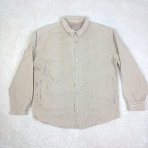 May include: A beige long-sleeved button-down shirt with a small embroidered logo on the left chest.