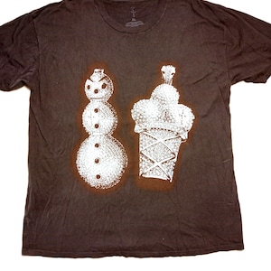 May include: A dark brown t-shirt featuring a white graphic of a snowman and an ice cream cone. The snowman has three round body sections and a carrot nose. The ice cream cone has a crown on top.
